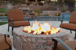 A cozy stone fire pit glowing with flames beside a pool and outdoor seating.