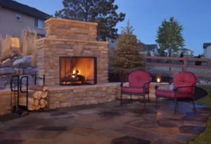 Cozy outdoor stone fireplace with seating under a clear evening sky.